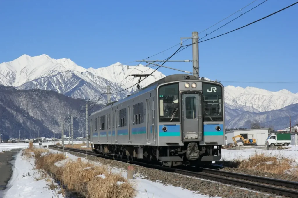 A train with a snowy backdrop of the Japanese alps.