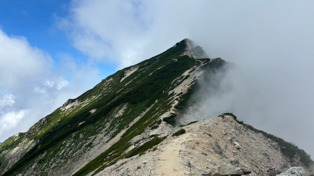 Clouds enshroud one side of the Karamatsu Mountain ridgeline with the summit in view in Hakuba Japan.