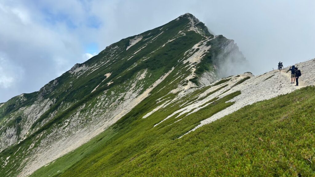 Hikers on the deep green and gravel Karamatsu ridgeline in August in Hakuba, Japan.