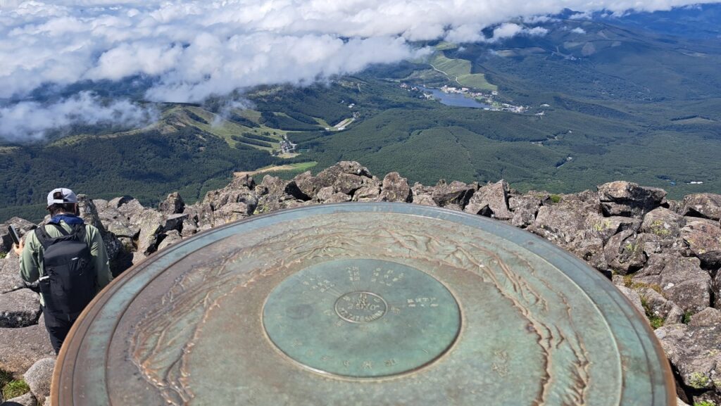 A dial shows surrounding mountains from the peak of Mt. Tateshina, with a village view below.