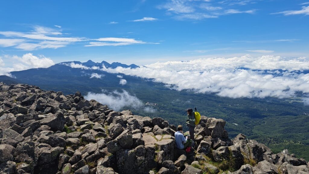 Hikers stand at the summit of Mt. Tateshina in Nagano, Japan with a view of Yatsugatake in the background.